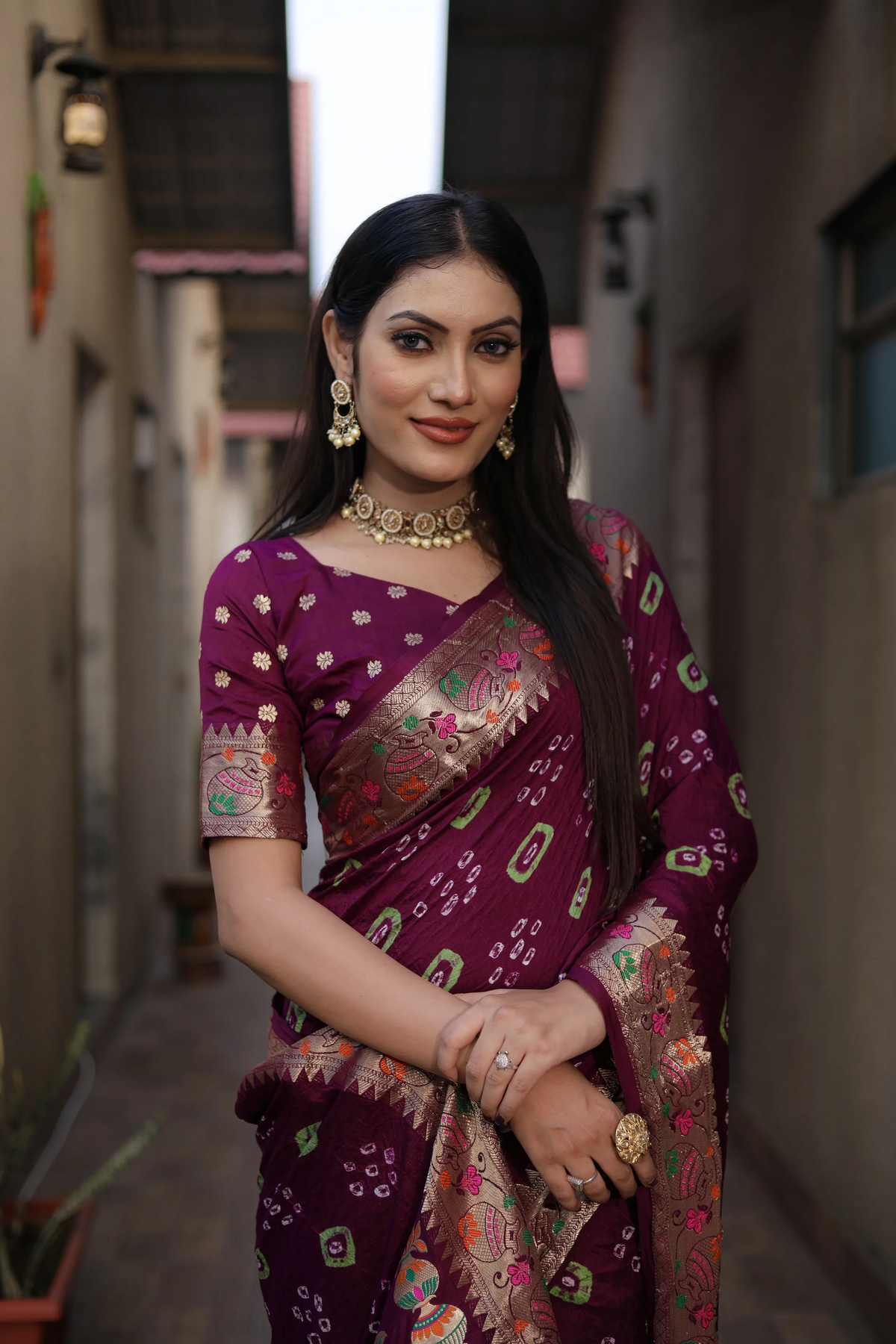 Woman in a purple saree with intricate patterns standing in an alleyway.