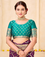Woman wearing a teal blouse with silver patterns and a purple saree against a beige background