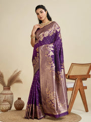 Woman wearing a purple and brown saree with floral patterns, standing in a room with decorative elements.