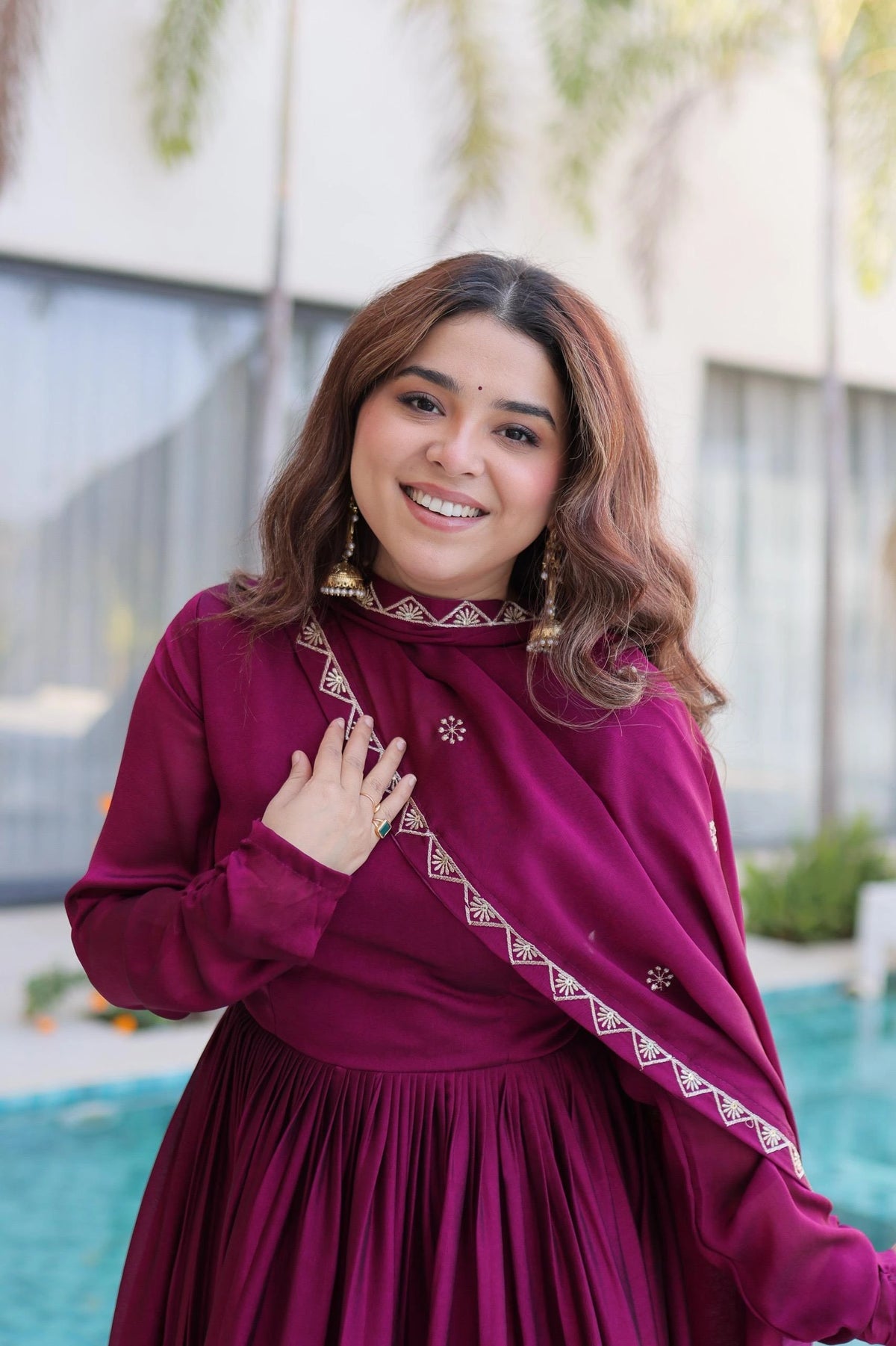Woman in a magenta traditional outfit with intricate designs, standing outdoors.