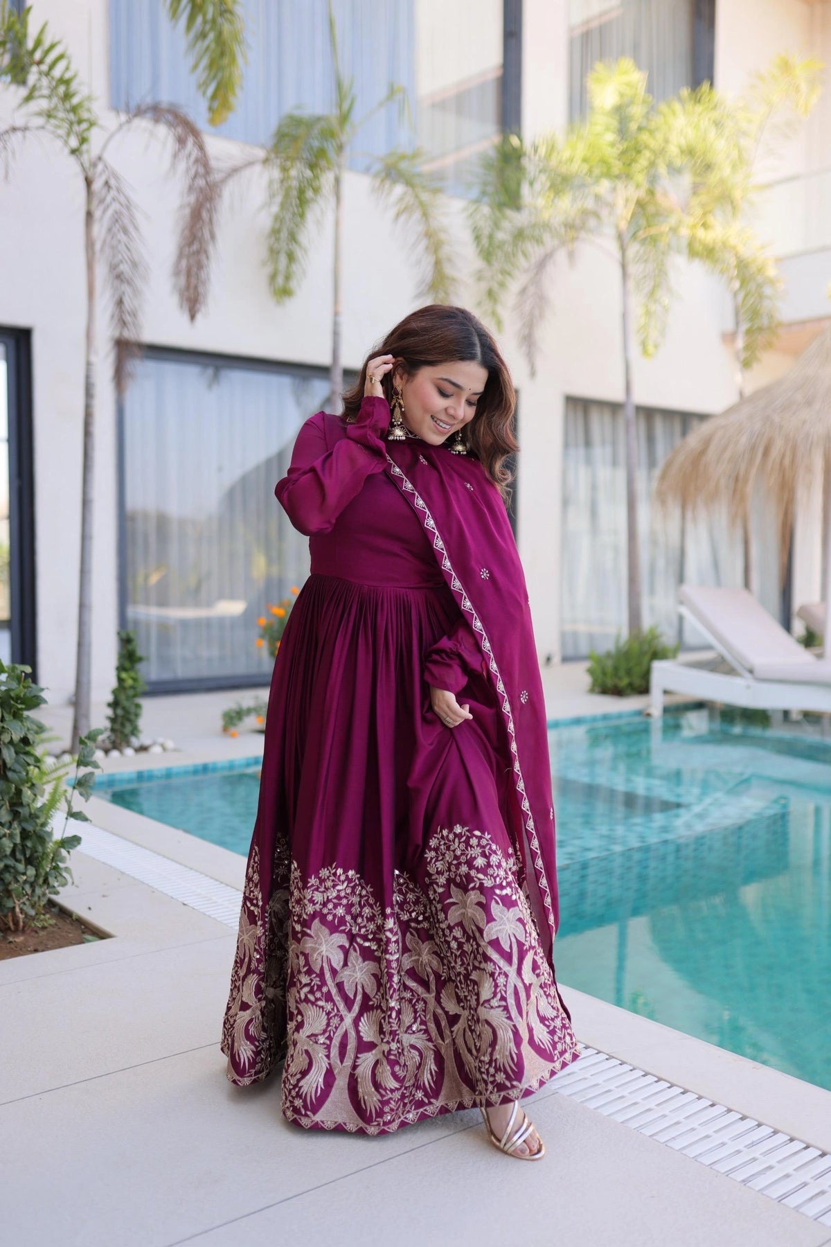 Woman in a magenta dress with white patterns standing by a poolside.