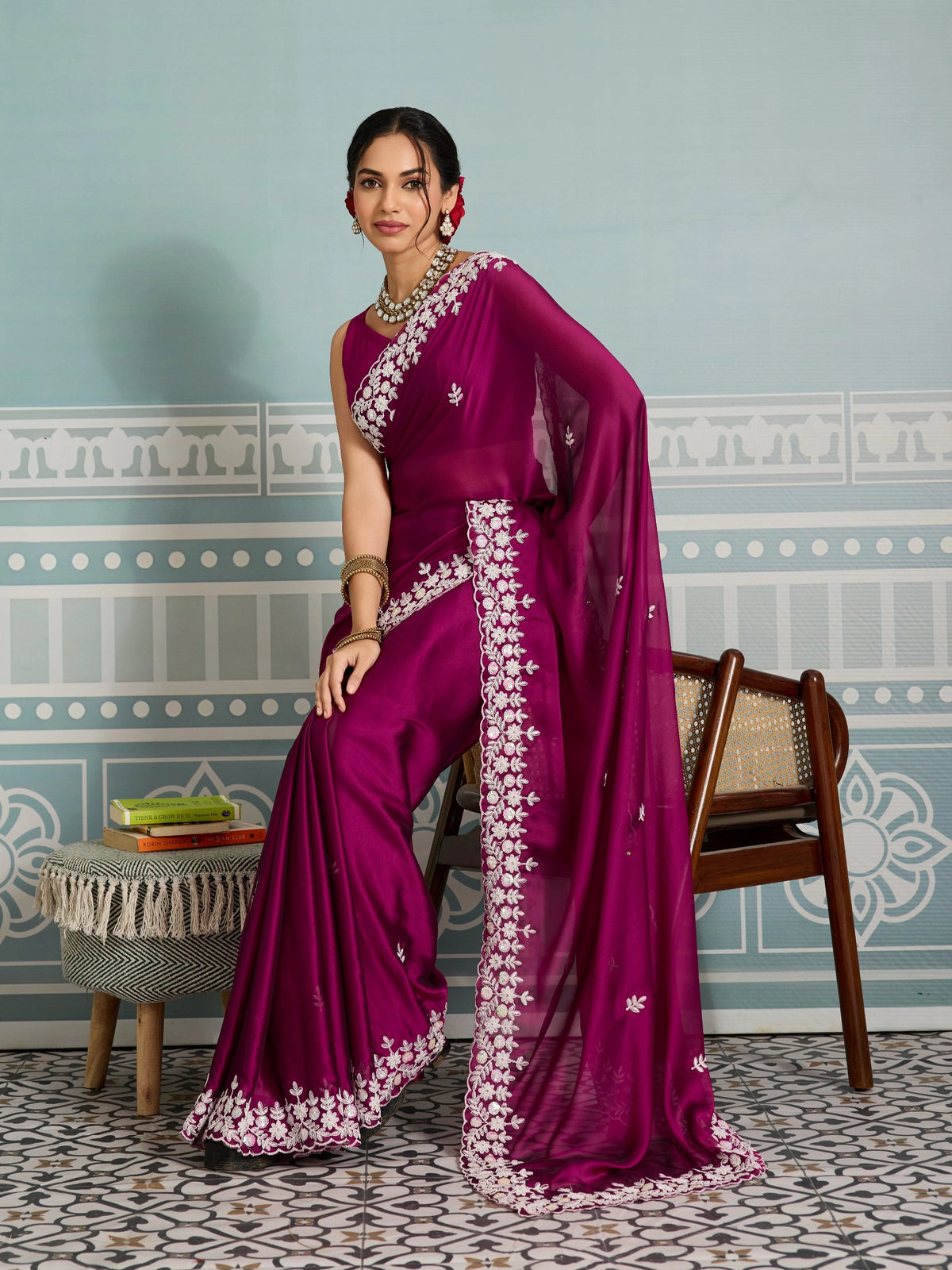 Woman in a purple saree with white patterns standing in a room with decorative walls and furniture.