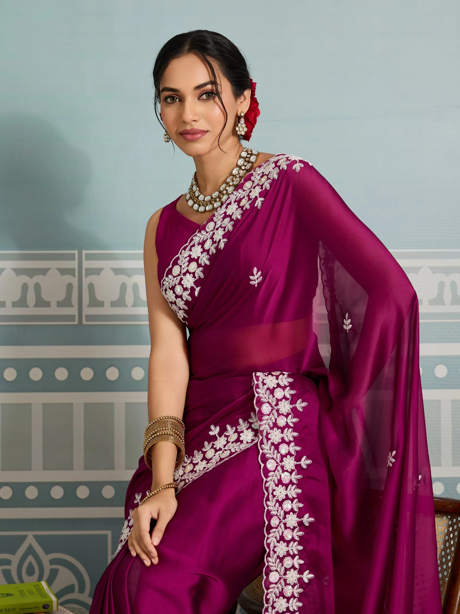 Woman wearing a purple saree with white embroidery against a decorative wall.