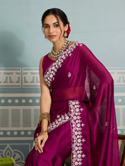 Woman wearing a purple saree with white embroidery against a decorative wall.