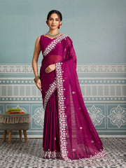 Woman wearing a magenta saree with white patterns in a room with decorative wall patterns.