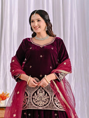 Woman wearing a maroon traditional outfit with intricate designs against a white curtain background