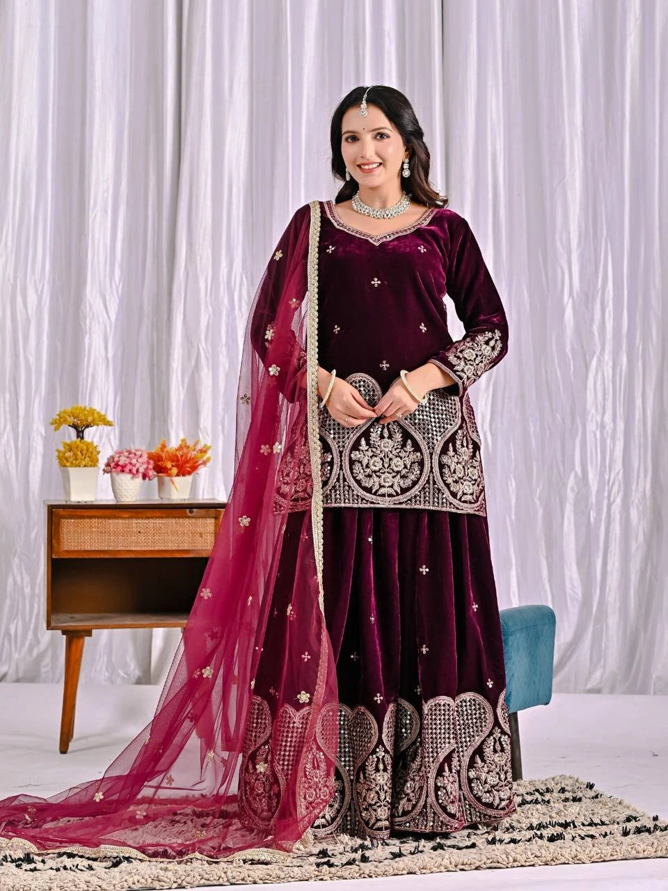 Woman in a maroon traditional outfit with pink dupatta against a white curtain background