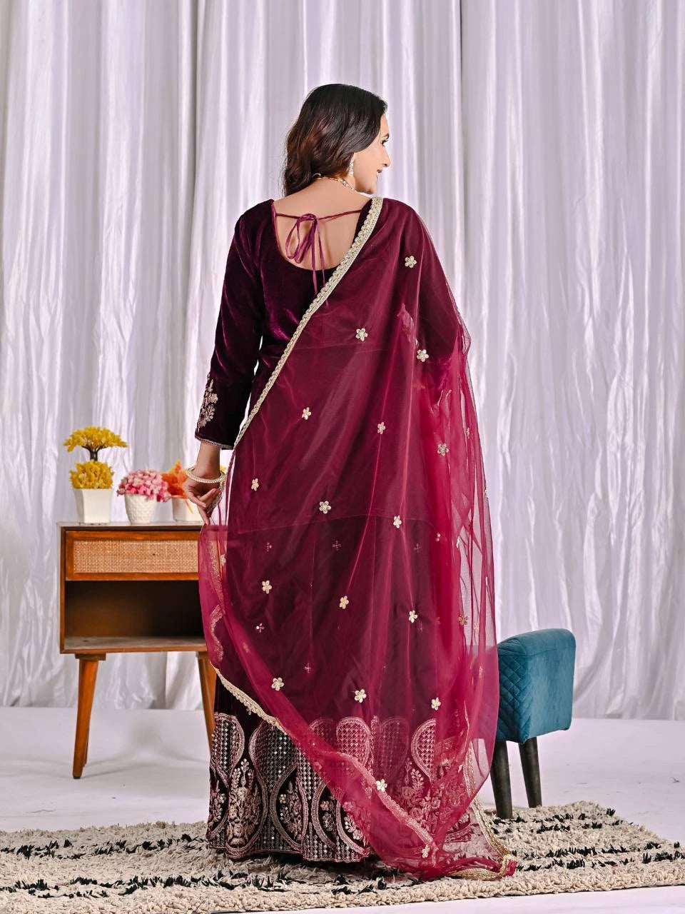 Woman wearing a maroon saree with gold details in a minimalistic setting.