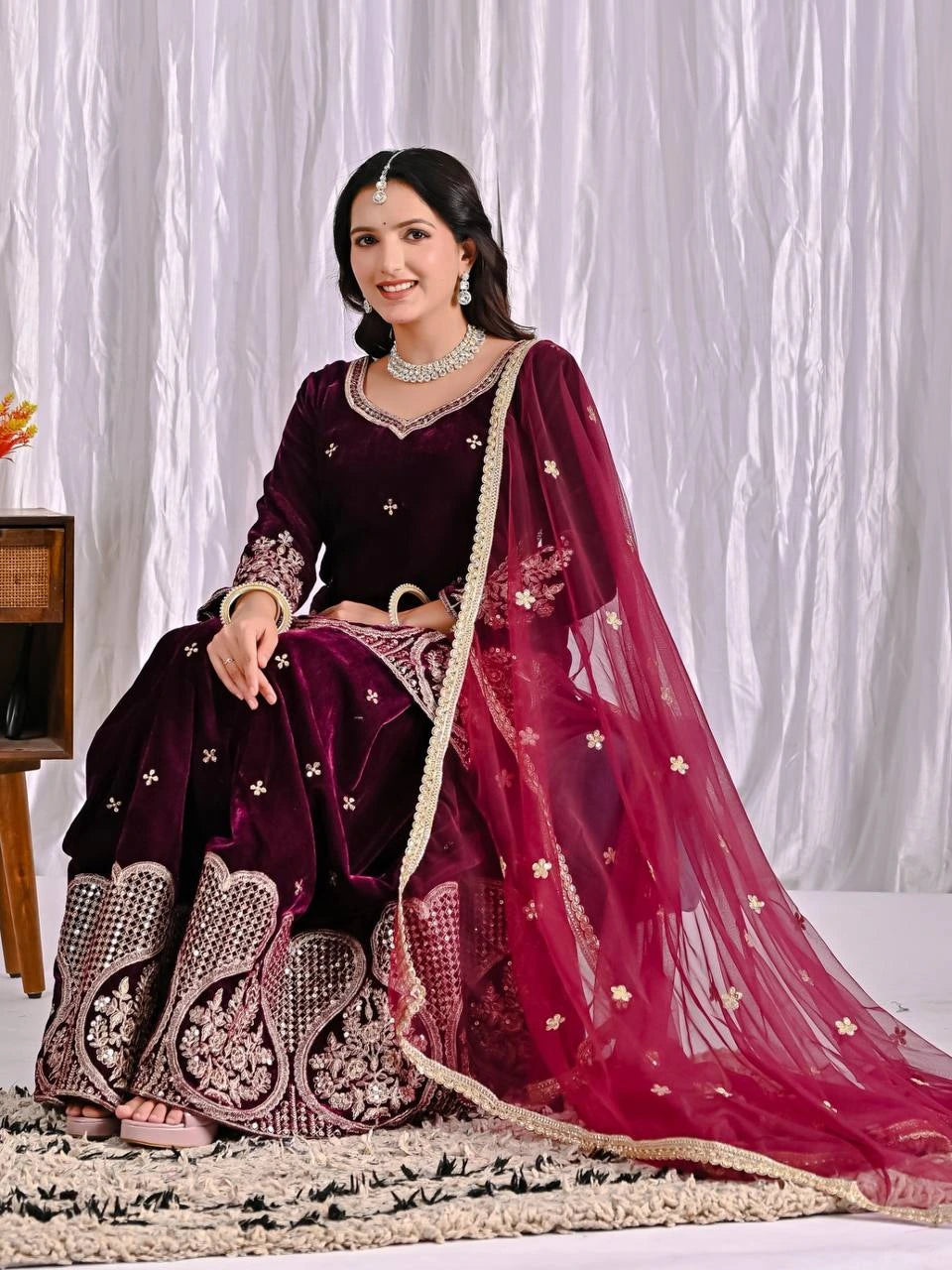 Woman in traditional maroon and pink embroidered outfit sitting on a white background