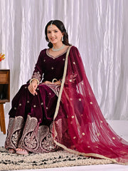 Woman in traditional maroon and pink embroidered outfit sitting on a white background