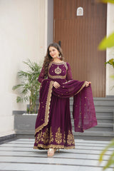 Woman in a purple traditional outfit with gold embroidery standing outside a building.