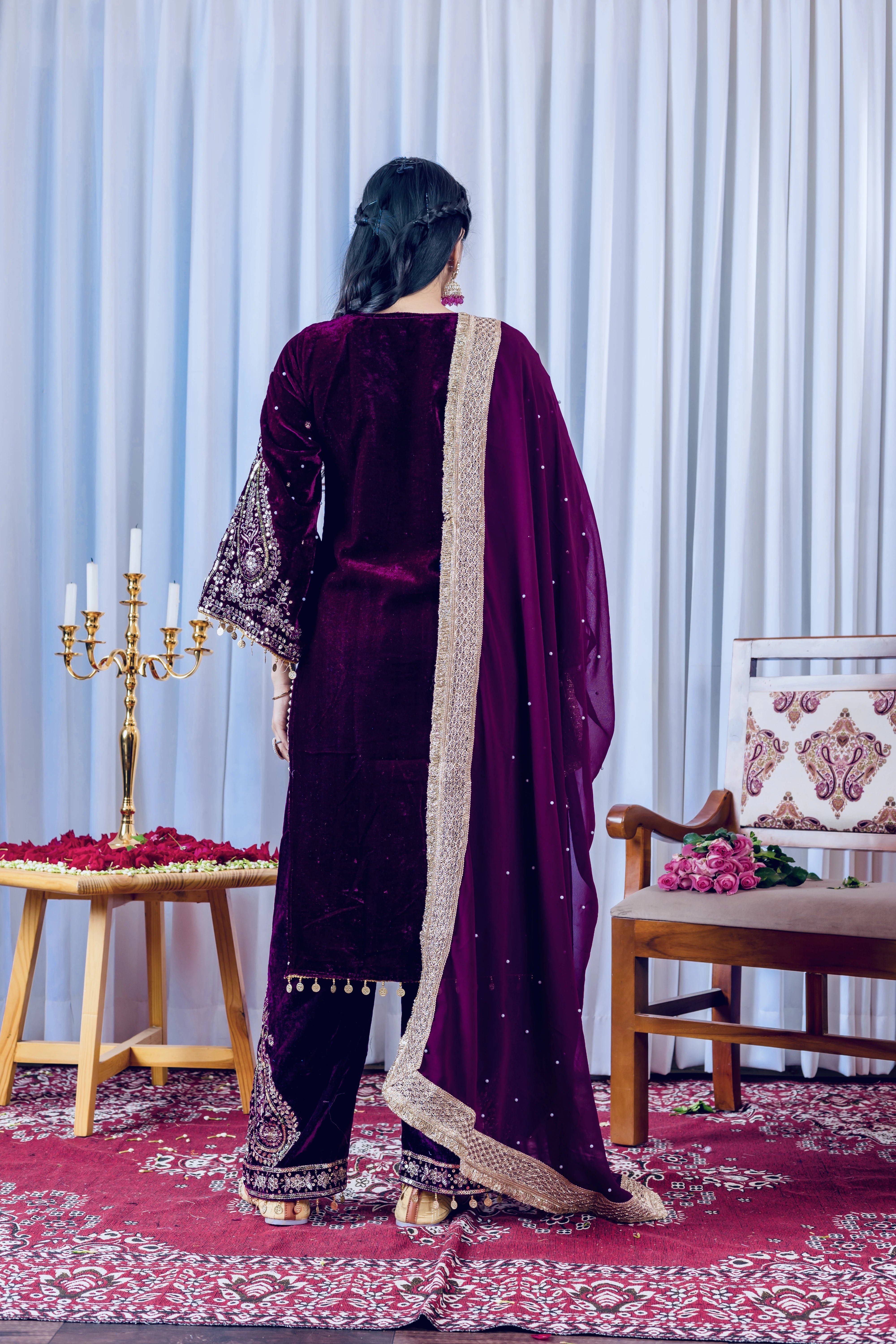 Person wearing a dark purple traditional outfit with gold details in a decorated room.