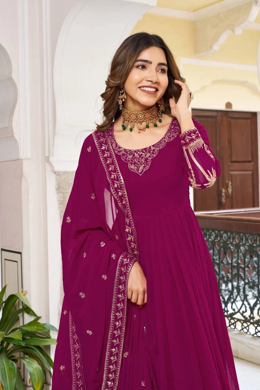 Woman in a purple traditional outfit with intricate designs standing in an ornate interior setting.