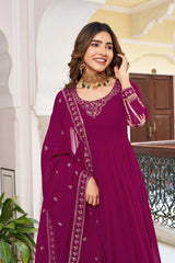 Woman in a purple traditional outfit with intricate designs standing in an ornate interior setting.