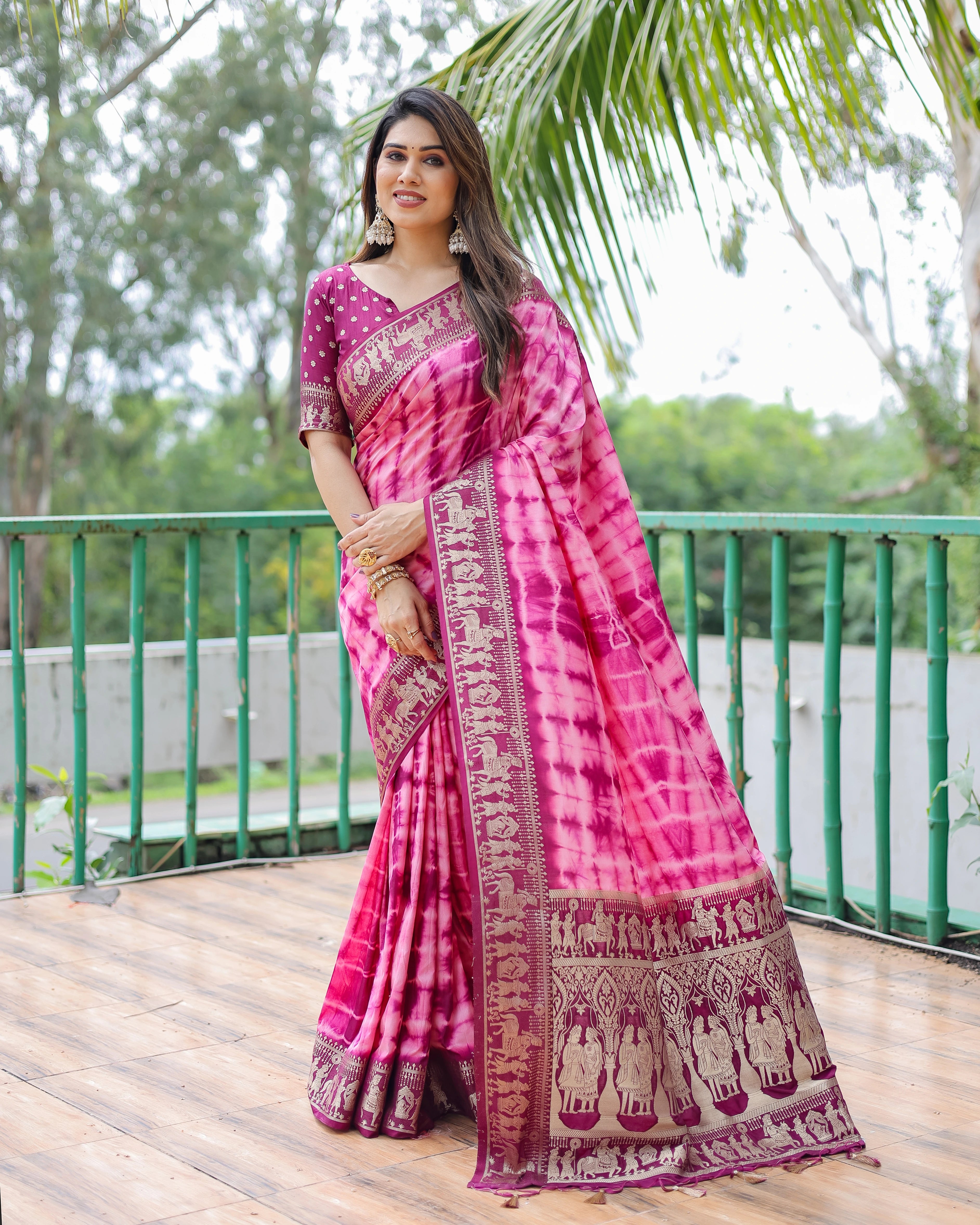 Woman wearing a pink saree with a traditional pattern on a wooden deck with greenery in the background