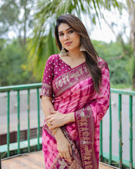Woman wearing a pink saree with a traditional design, standing outdoors with greenery in the background.