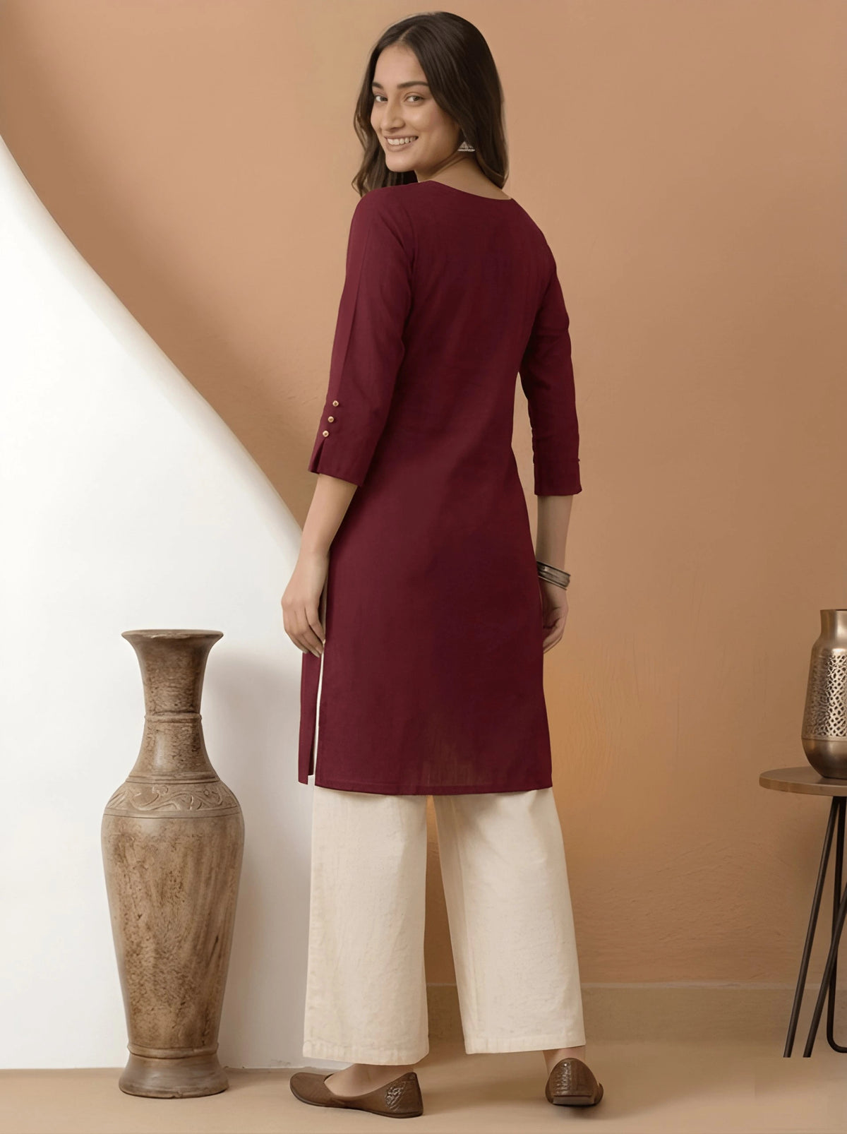 Woman wearing a maroon kurta with white pants against a beige wall.