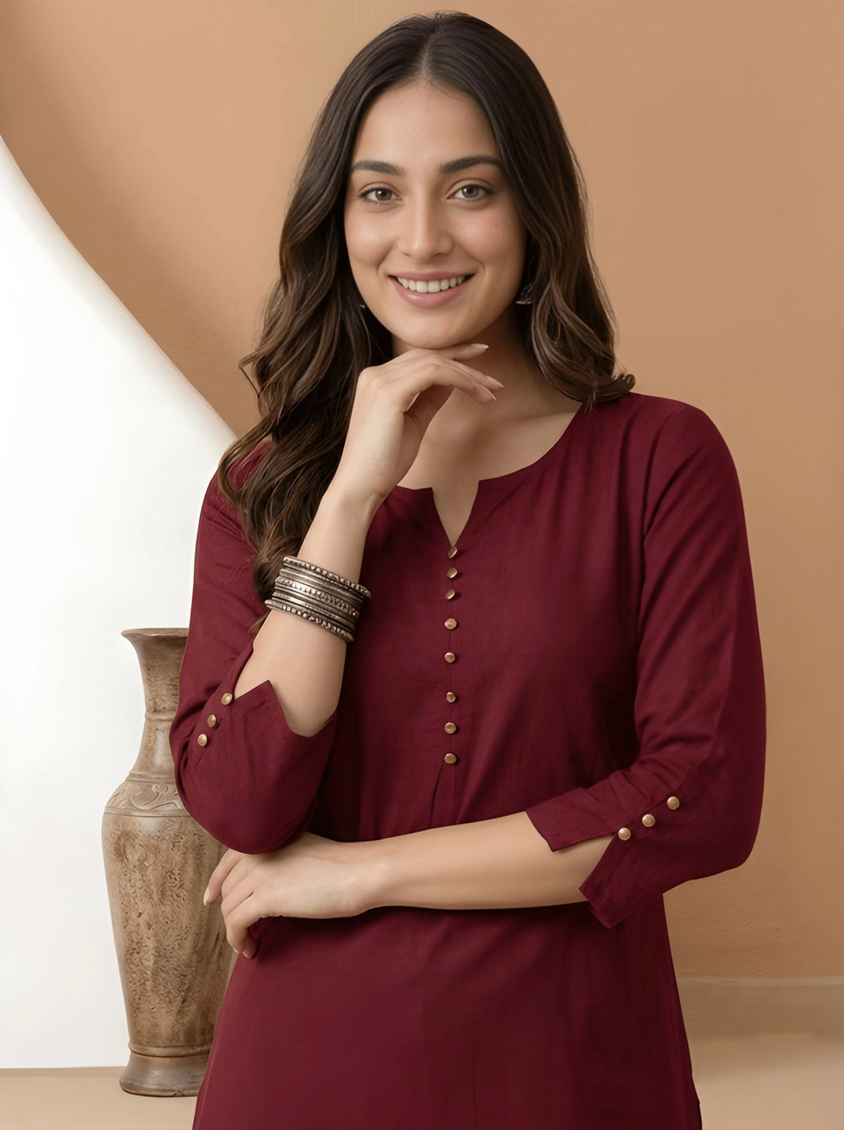 Woman wearing a burgundy dress with gold buttons against a beige background