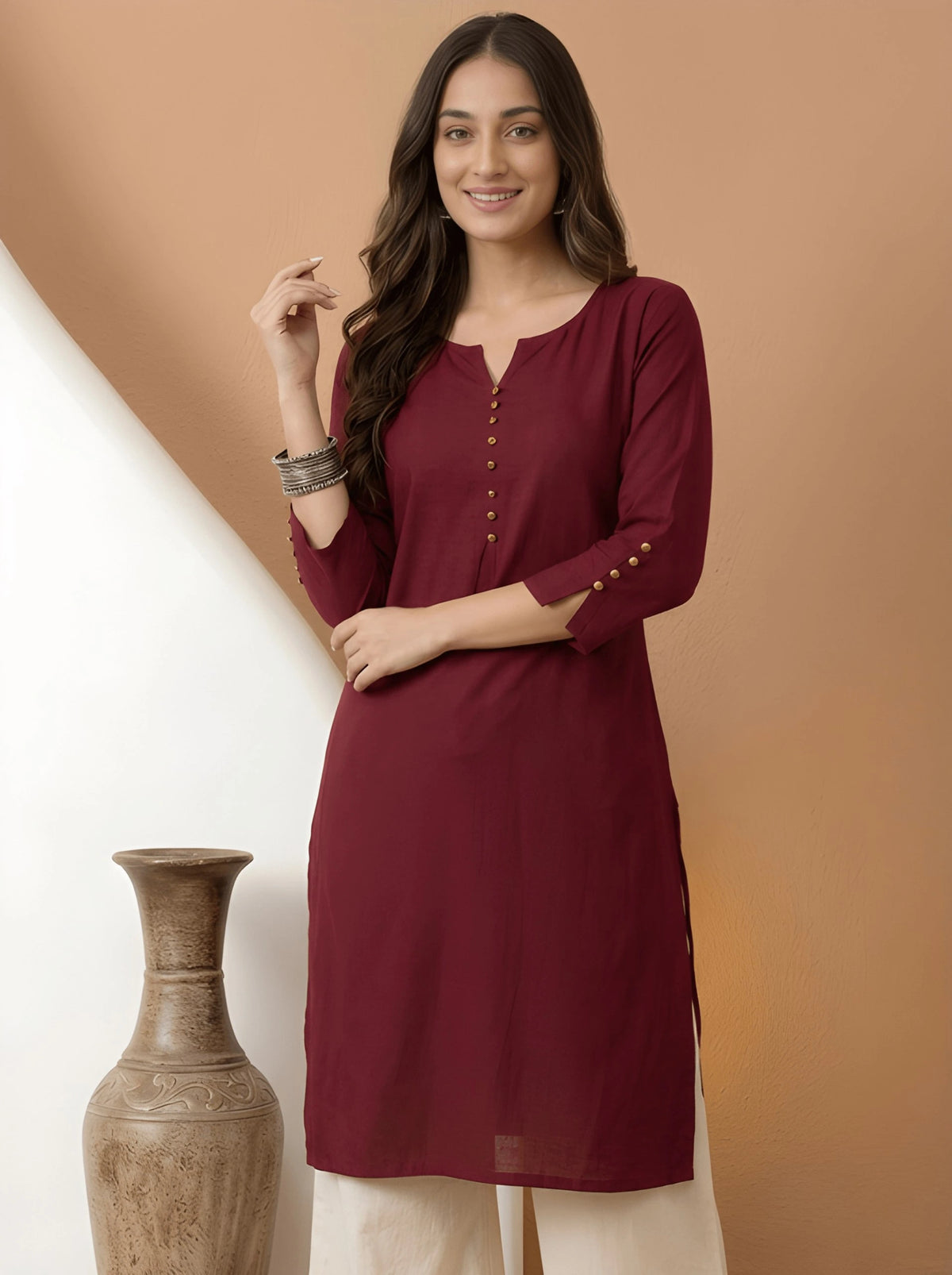 Woman wearing a maroon kurta with beige pants against a brown background