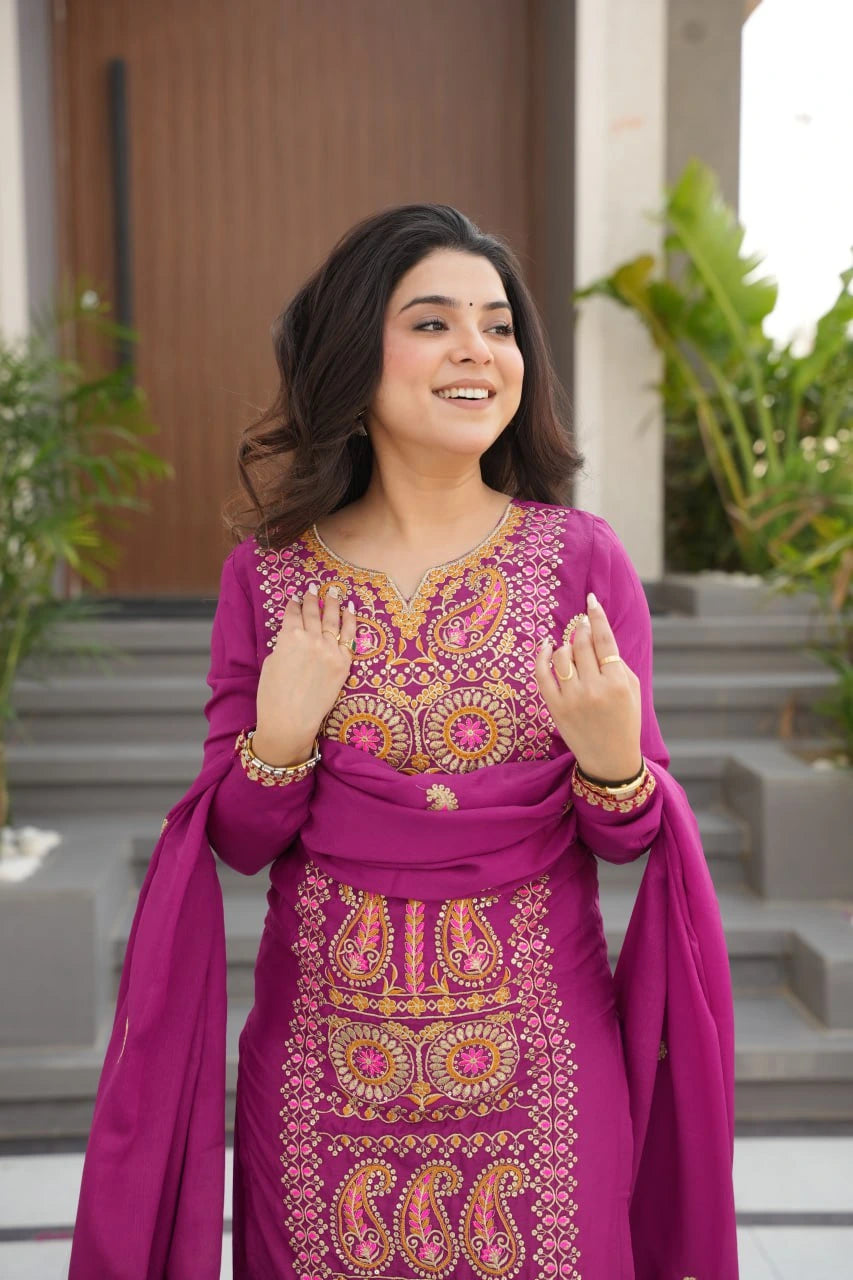 Woman in a traditional embroidered outfit standing outdoors with plants and steps in the background