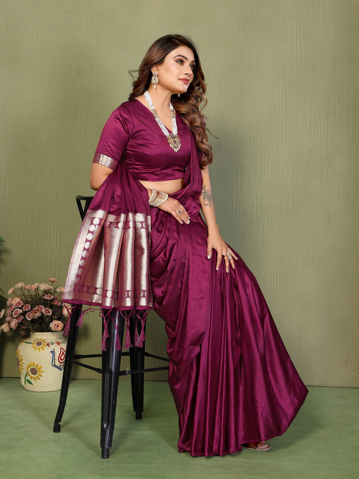 Woman in a purple saree sitting on a chair against a green background
