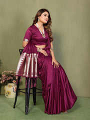 Woman in a purple saree sitting on a chair against a green background