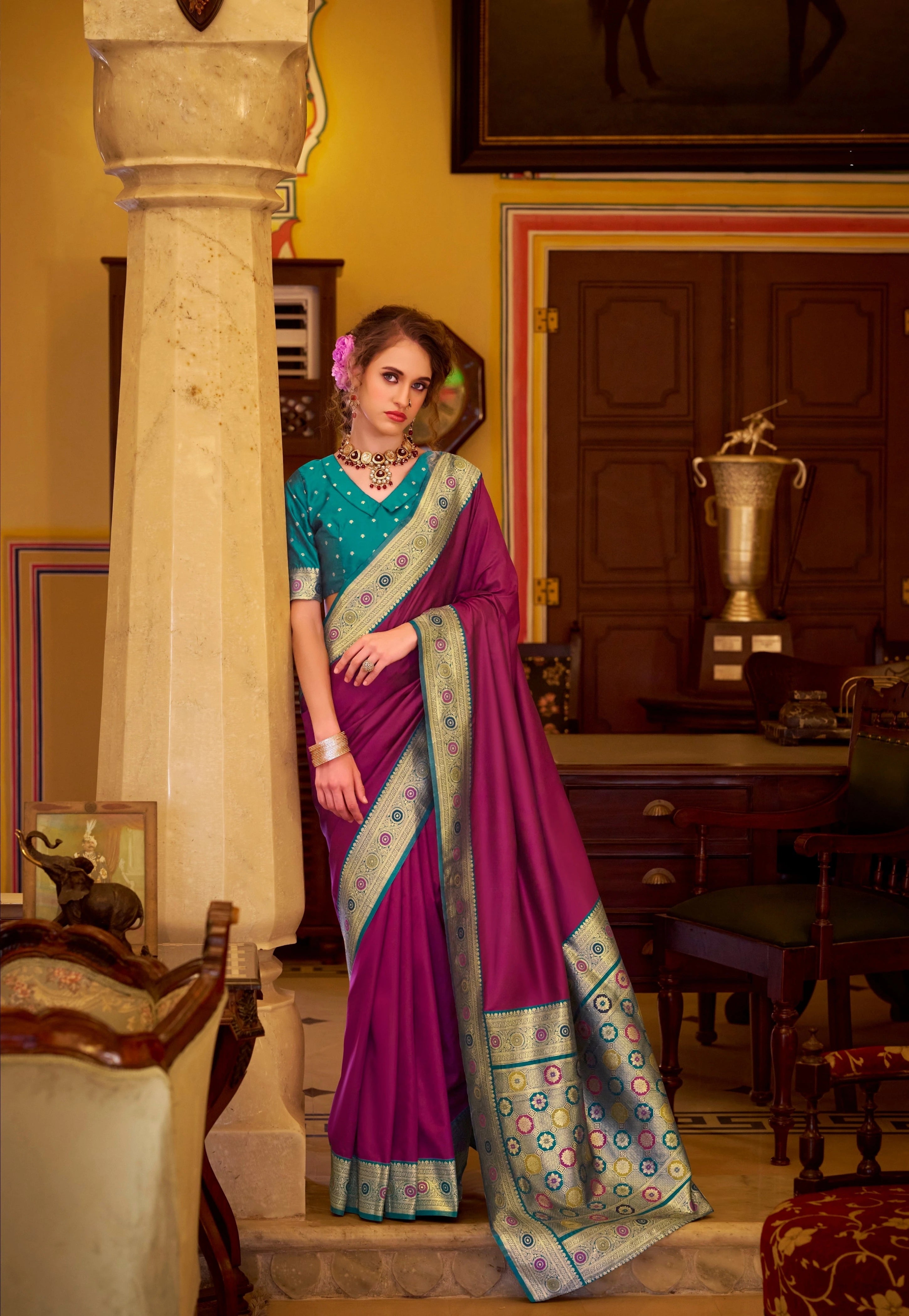 Woman in a traditional saree standing in an elegant room with decor elements.