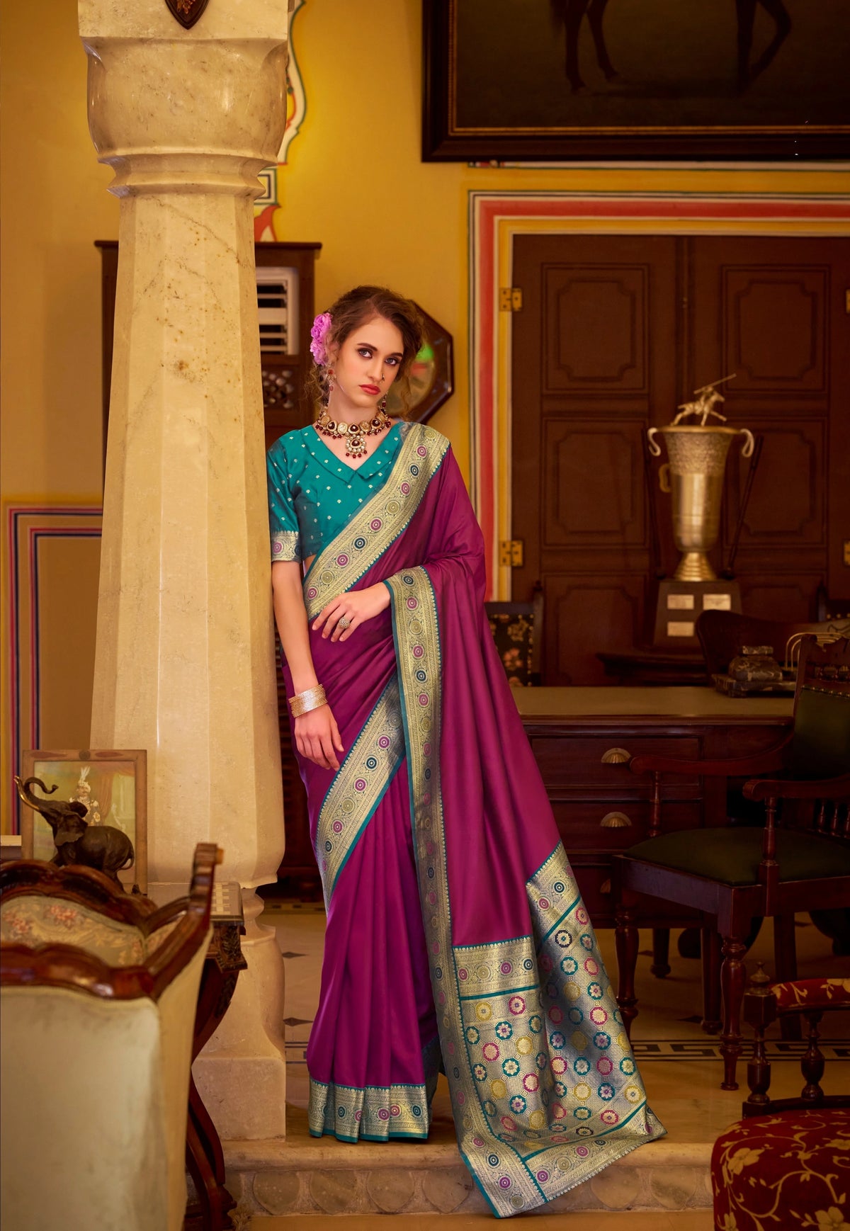 Woman in a traditional saree standing in an elegant room with decor elements.