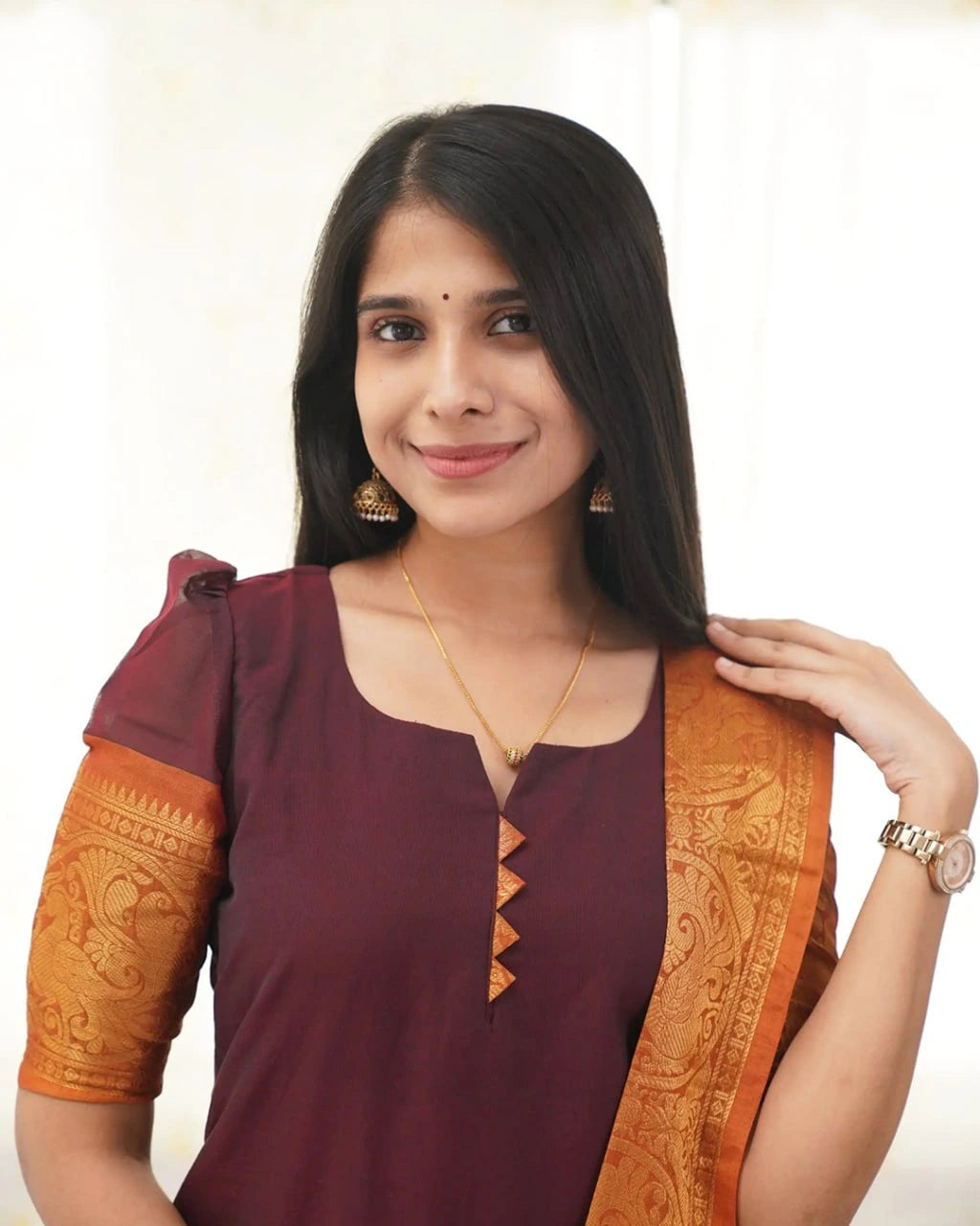 Woman wearing a maroon and orange traditional outfit with a plain background
