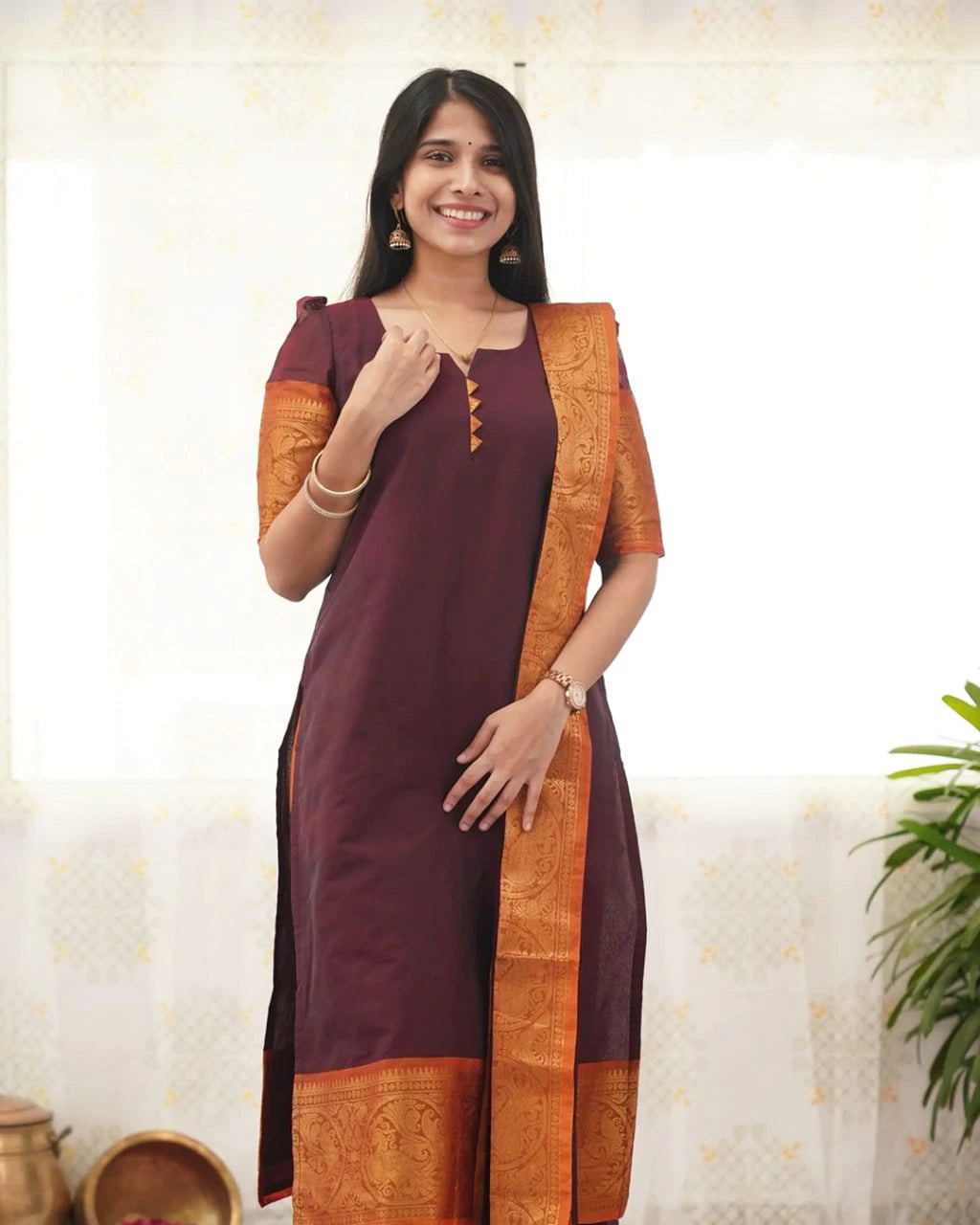 Woman wearing a maroon and orange traditional outfit with a plant in the background