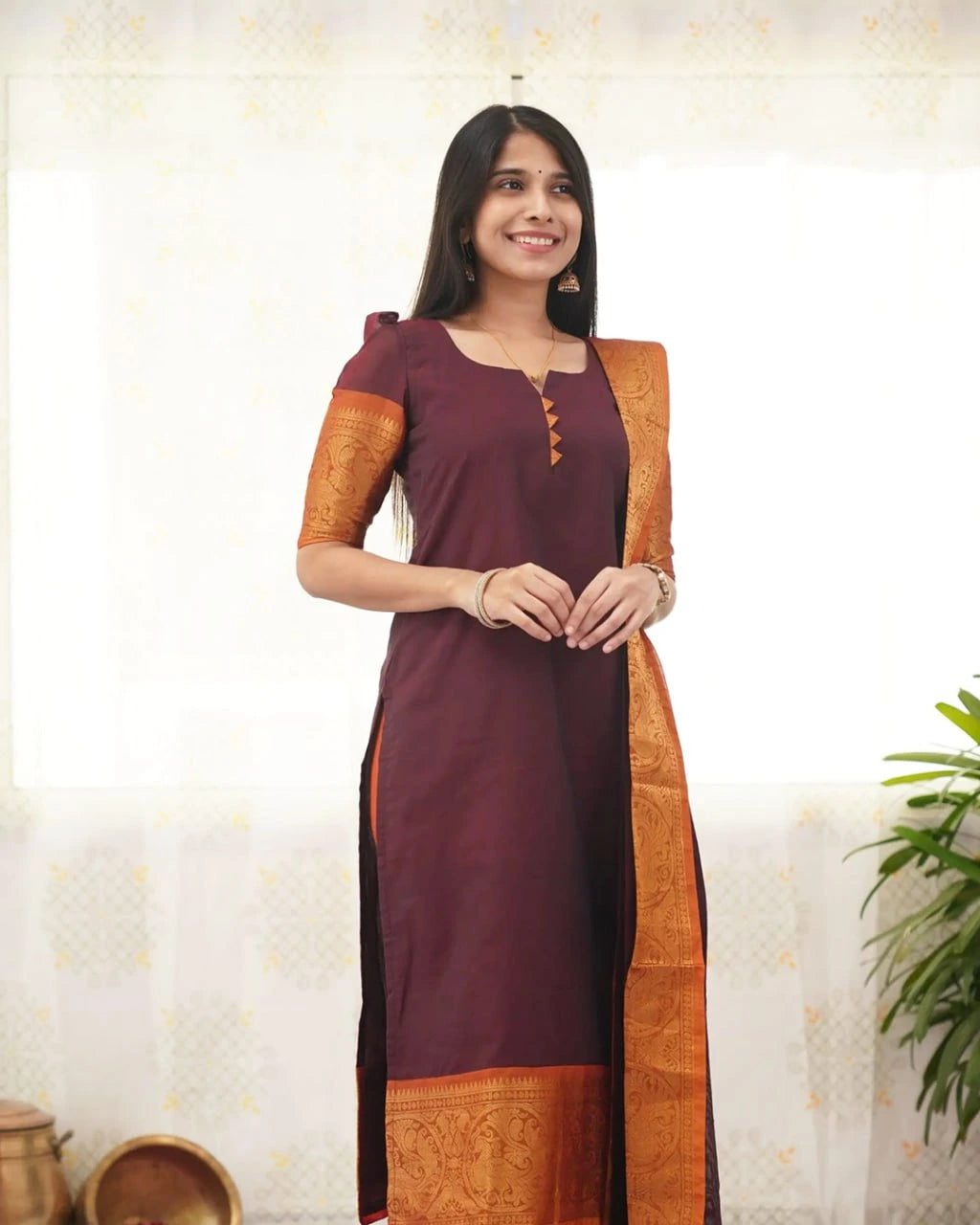 Woman wearing a maroon and orange traditional outfit with a white curtain background