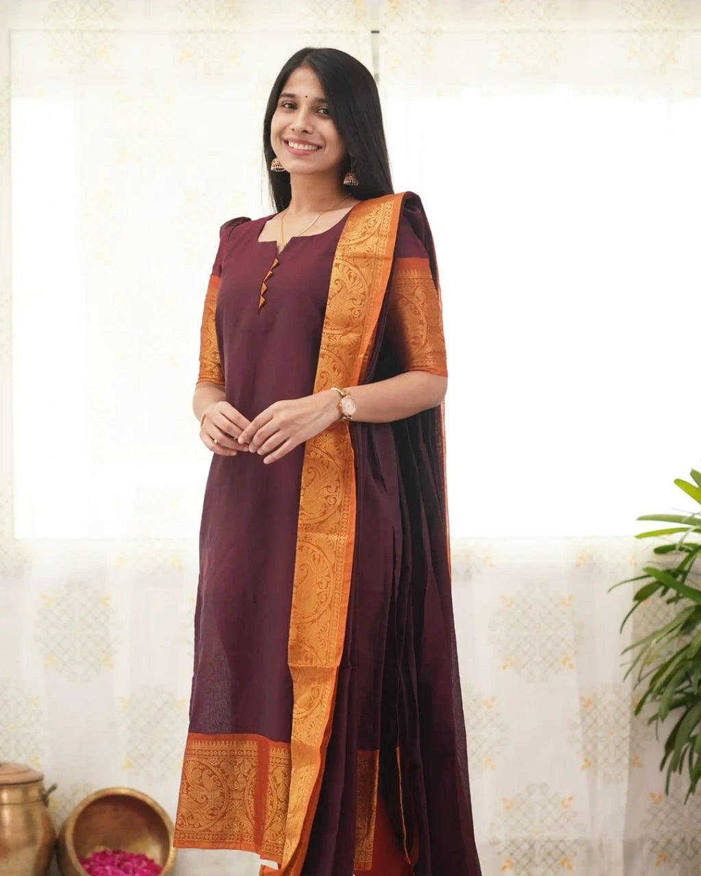 Woman wearing a maroon kurta with an orange and black border against a light background