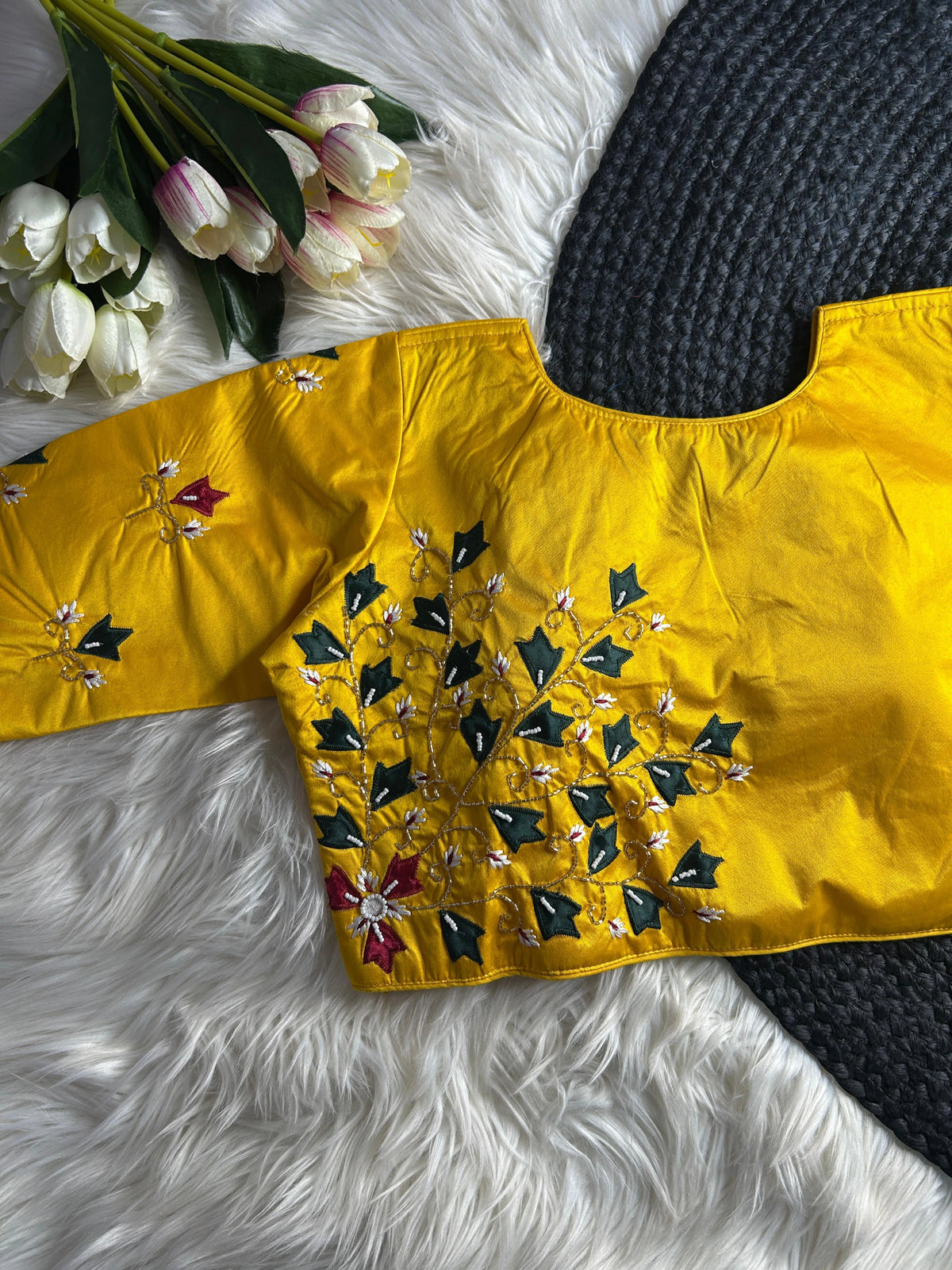 Yellow embroidered top on a textured surface with flowers in the background