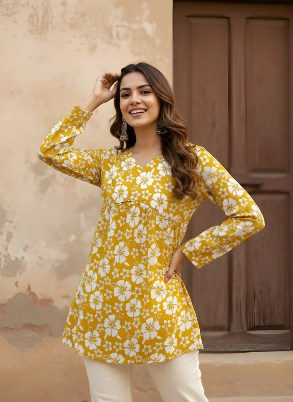 A medium shot of the woman posing with one hand on her head, showcasing the V-neckline and the empire-waist gathering of the kurti. Her long, wavy brown hair and large silver jhumka earrings complement the ethnic look.