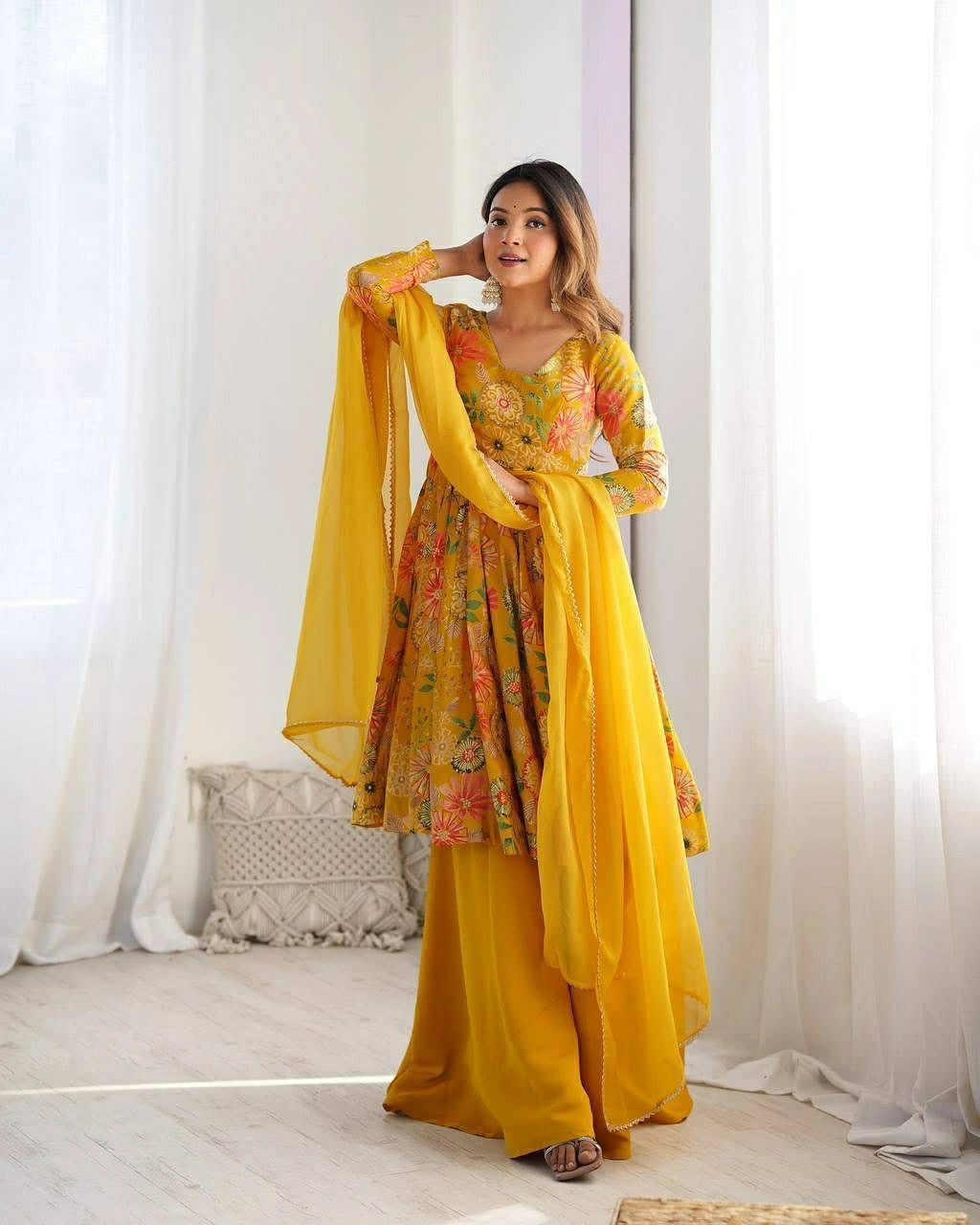 Woman in a yellow floral dress standing in a bright room with white curtains.