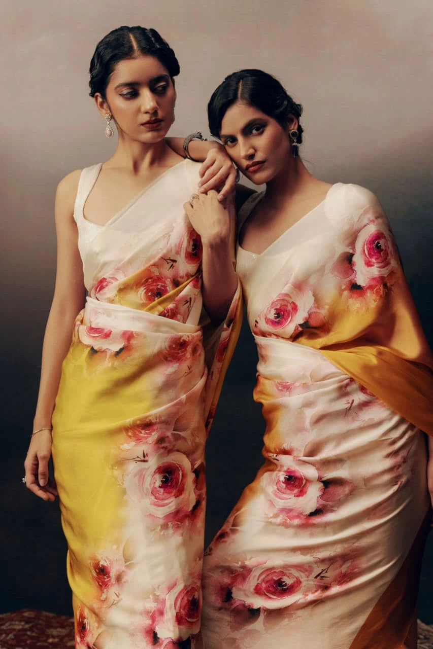 Two women wearing floral sarees with a neutral background