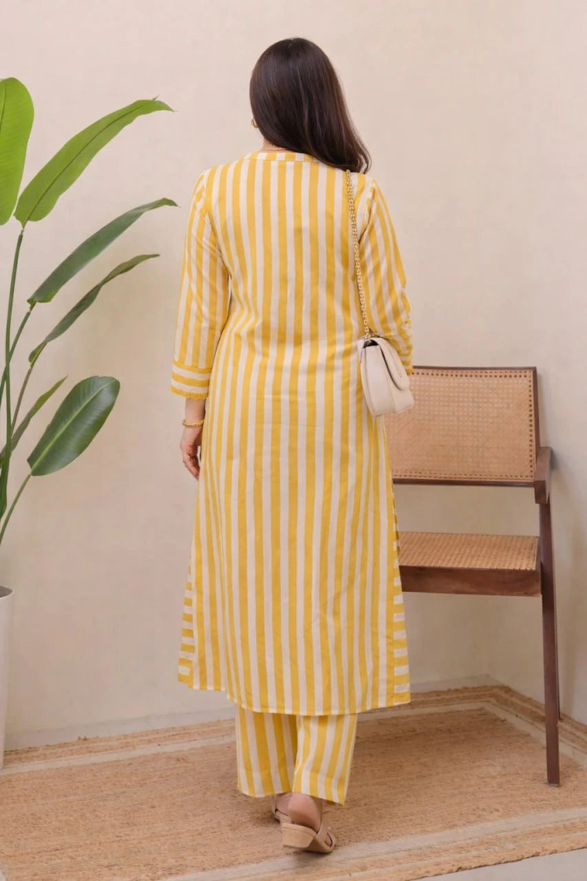 Woman wearing a yellow and white striped outfit standing in a room with a plant and wooden furniture.