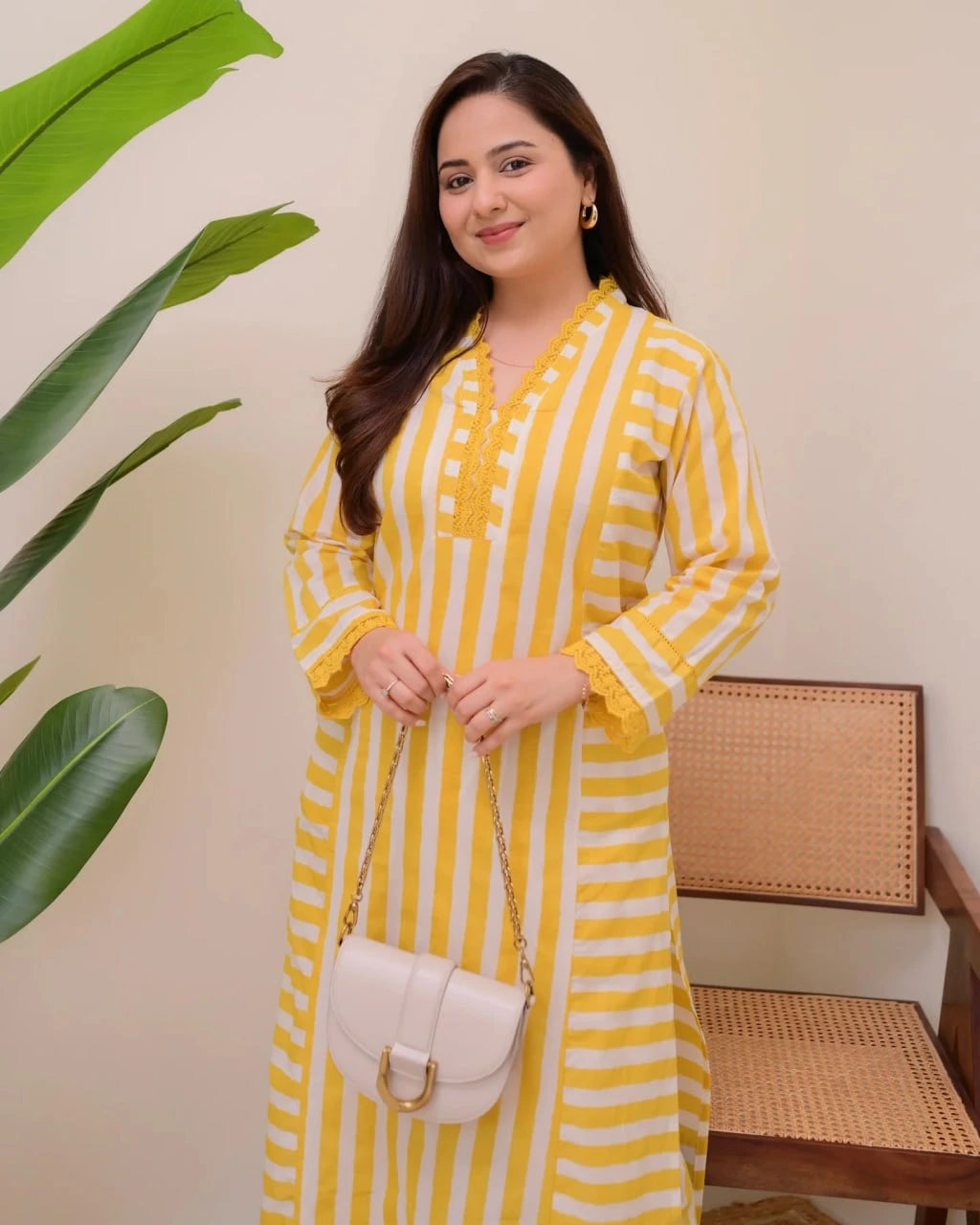 Woman wearing a yellow and white striped dress holding a white handbag indoors.