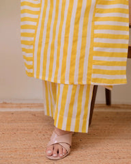 Yellow and white striped skirt worn by a person on a wooden floor.