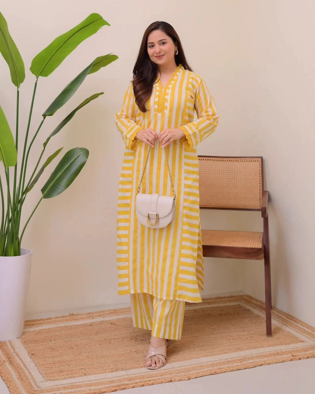 Woman in a yellow striped outfit standing in a room with a plant and chair.