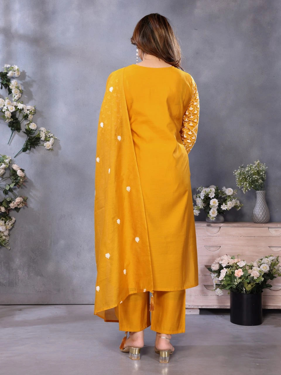 Woman wearing a mustard yellow traditional outfit with white polka dots in a decorative setting.