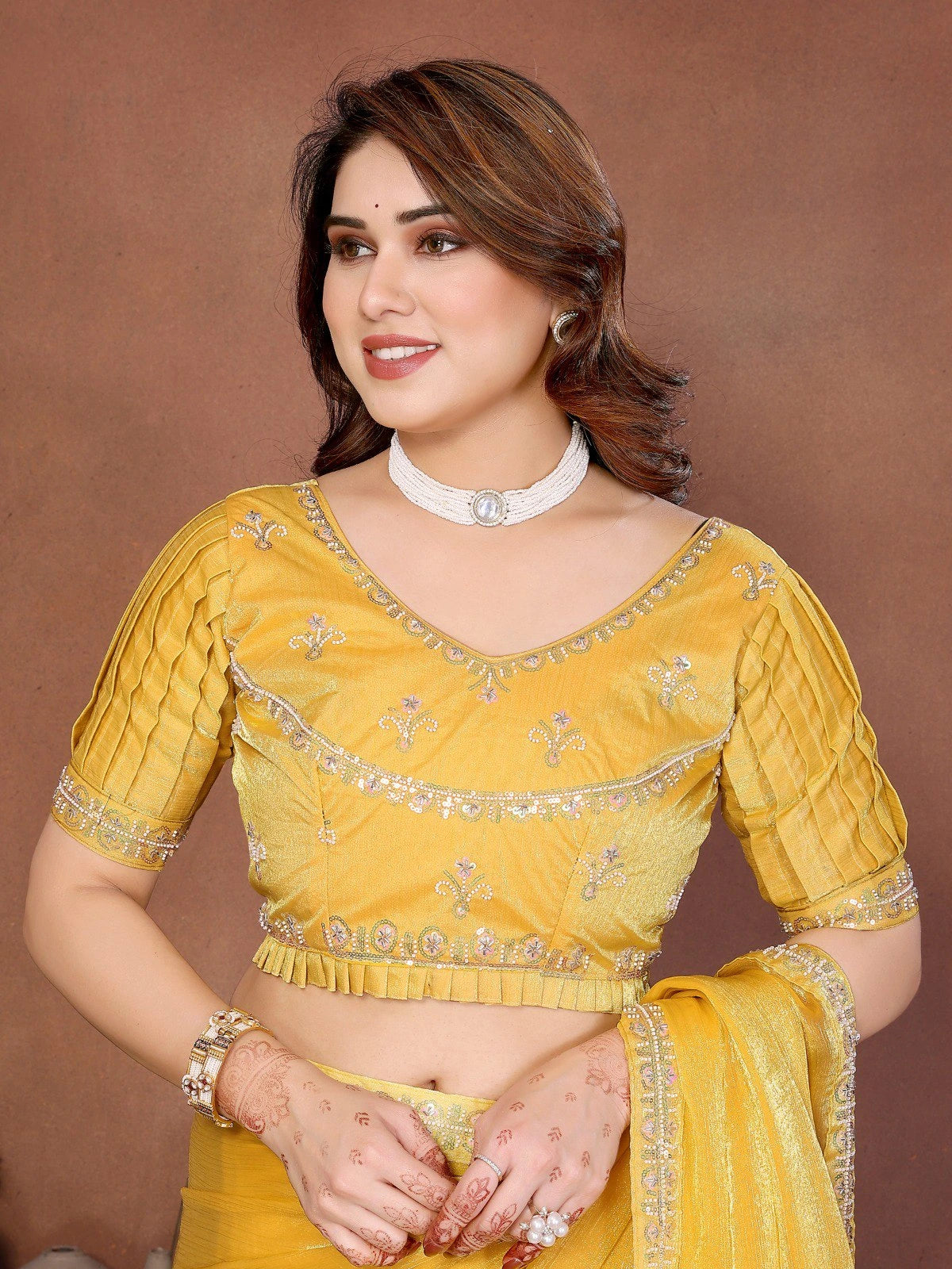 Woman wearing a yellow embroidered blouse with a matching saree against a brown background