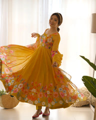 Woman in a yellow floral dress standing in a bright room with white curtains.