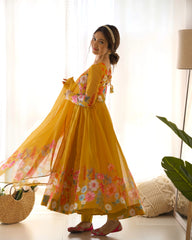 Woman wearing a yellow floral dress standing in a bright room with white curtains.
