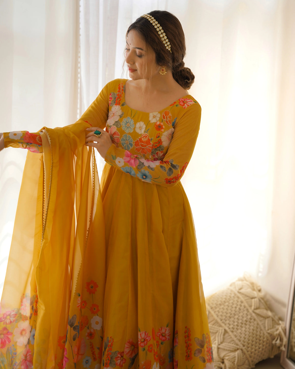 Woman in a yellow floral dress holding a dupatta against a white curtain background