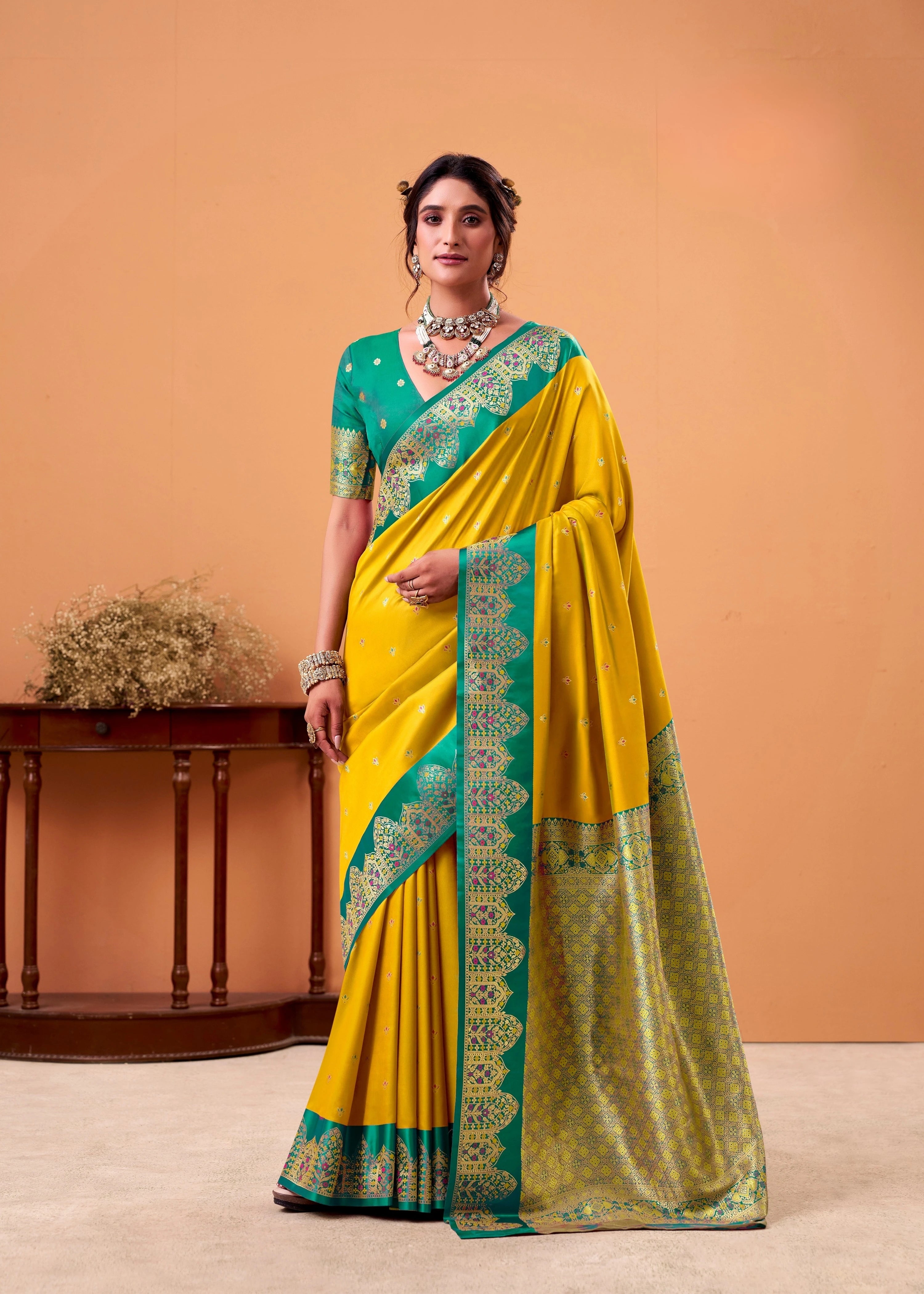 Woman wearing a yellow saree with green border against an orange background