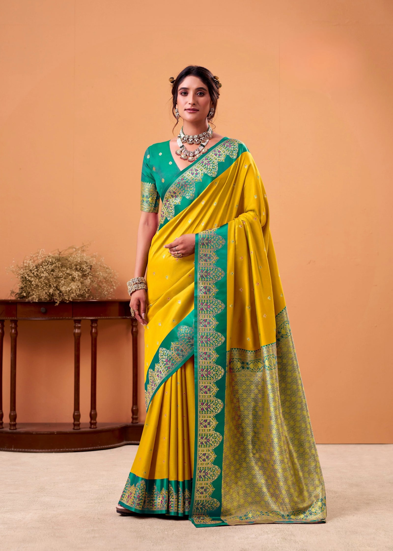 Woman wearing a yellow saree with green border against an orange background