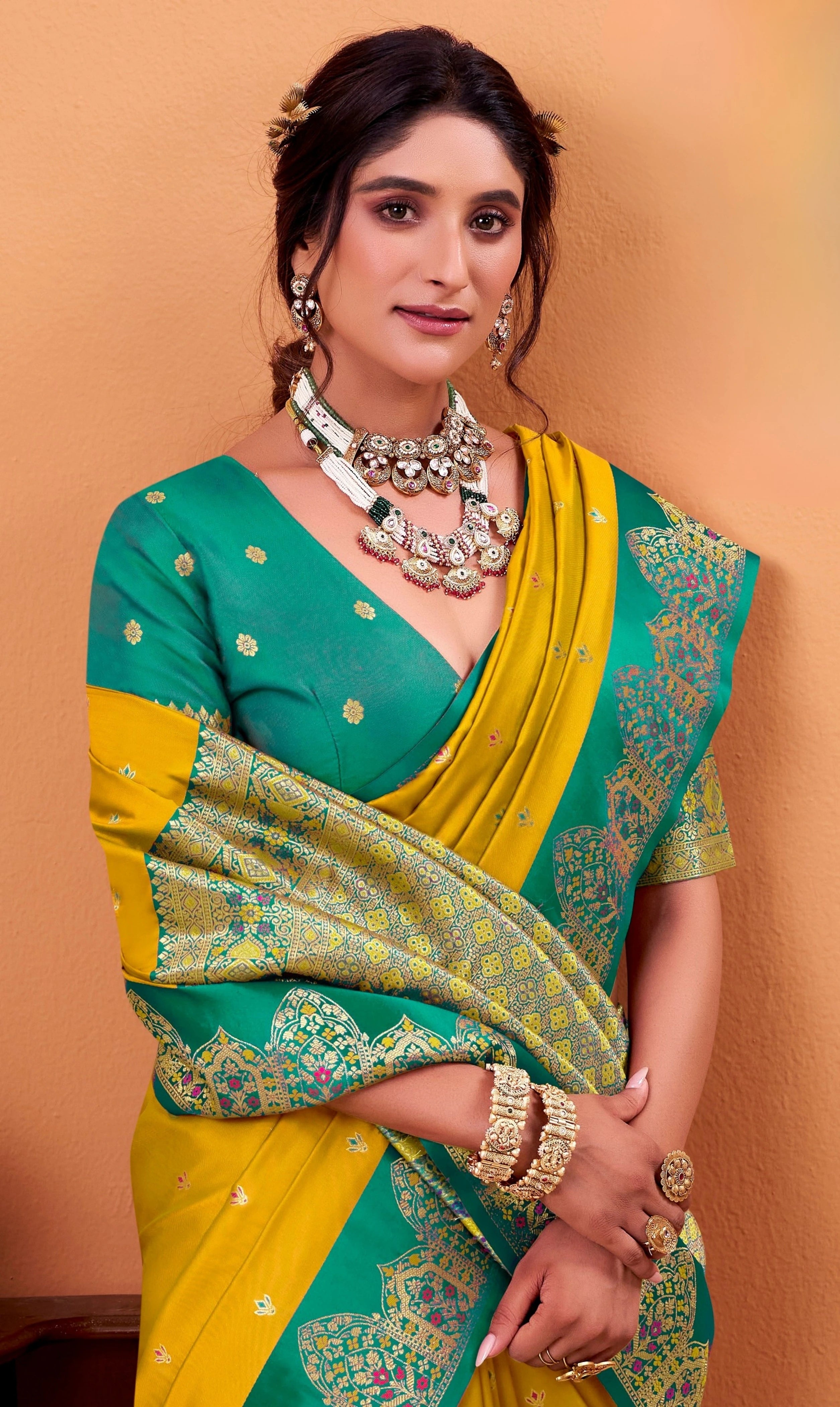 Woman wearing a green and yellow saree with jewelry against an orange background