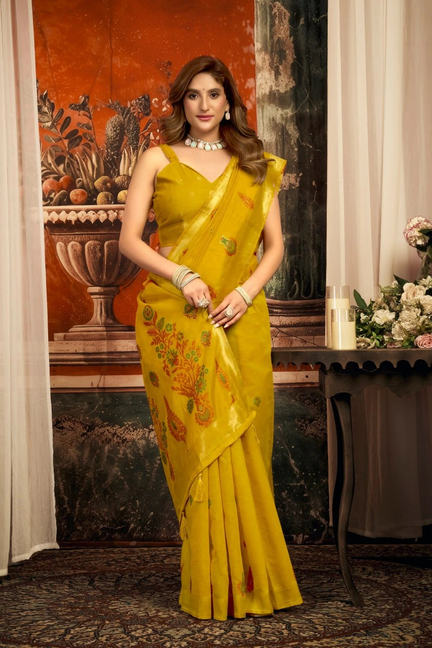 Woman in a yellow saree with floral patterns standing indoors.