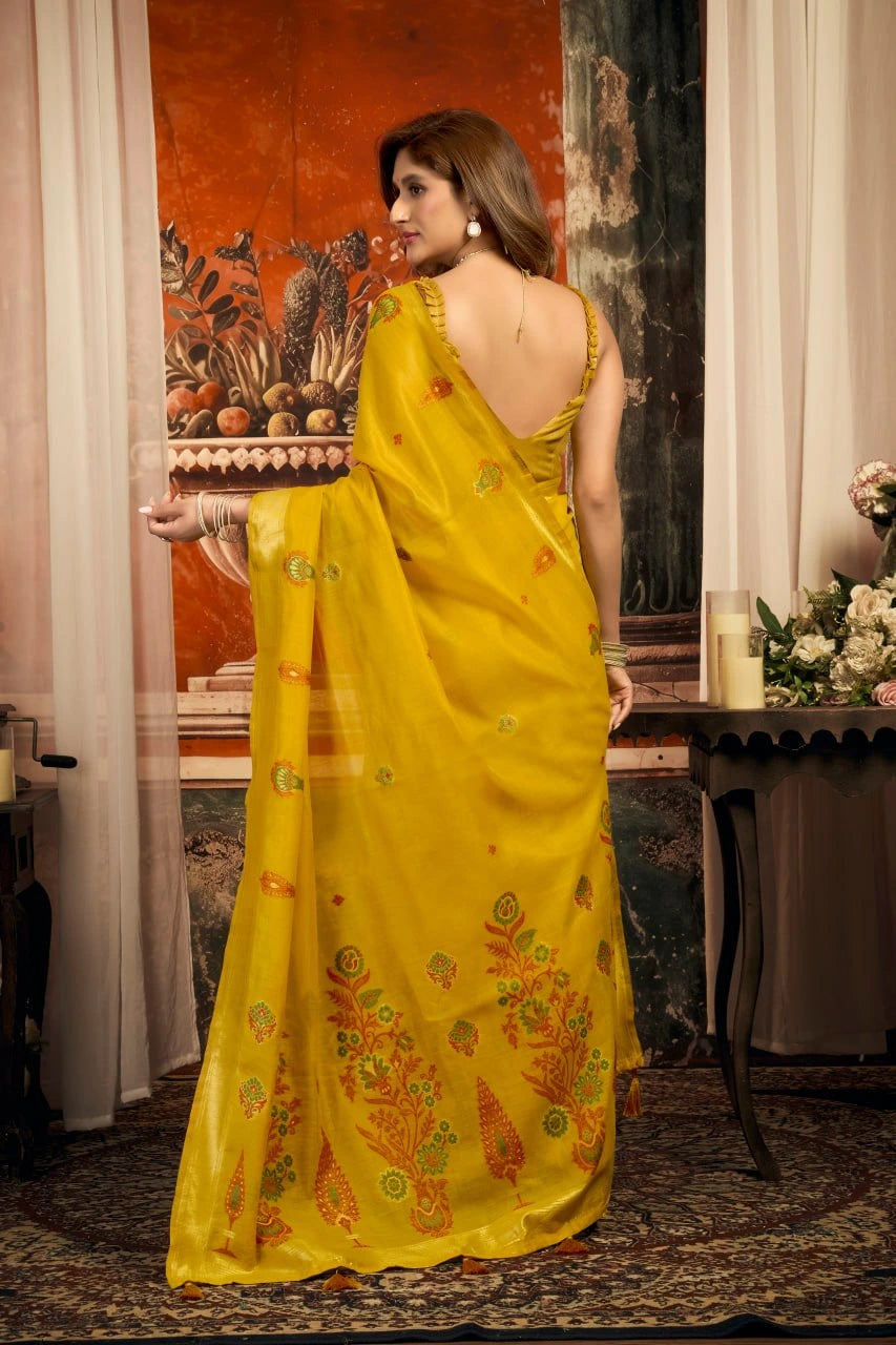 Woman in a yellow saree with floral patterns standing indoors.